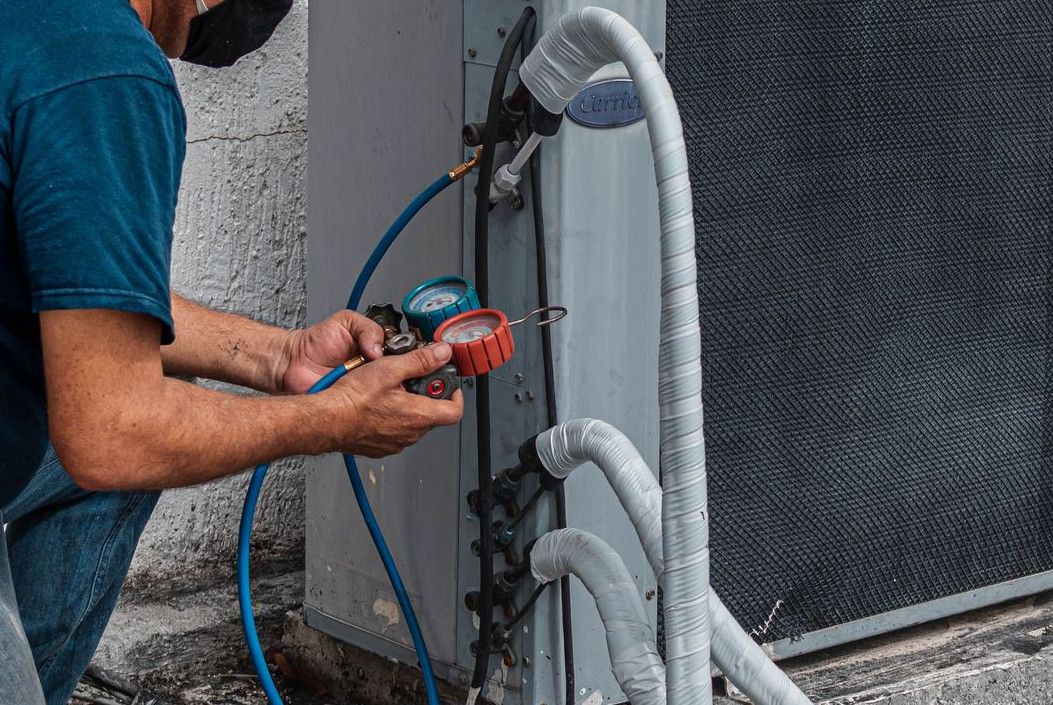 Technician repairing an air conditioner unit outdoors, wearing a facemask and using a manifold gauge.